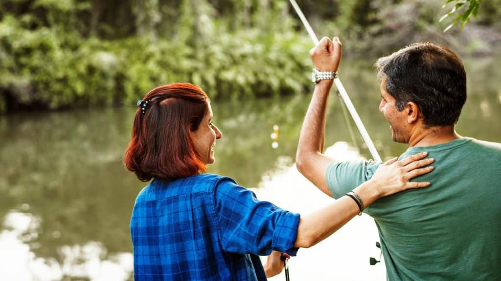 A couple fishing by a lake, smiling and celebrating a catch.