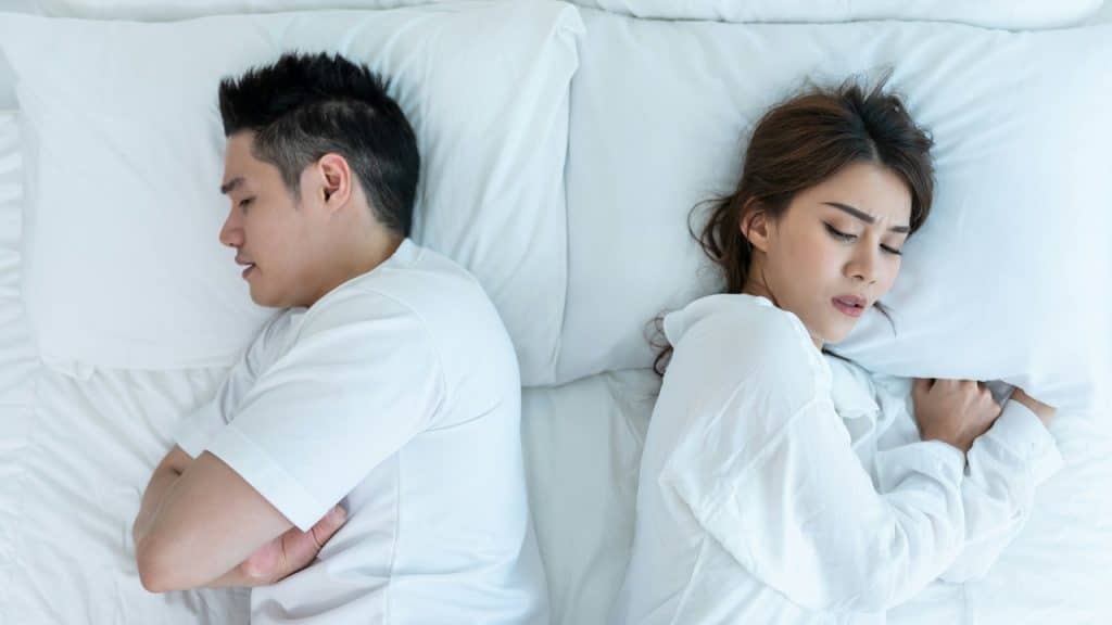 A couple lying next to each other on a bed and not looking at each other.