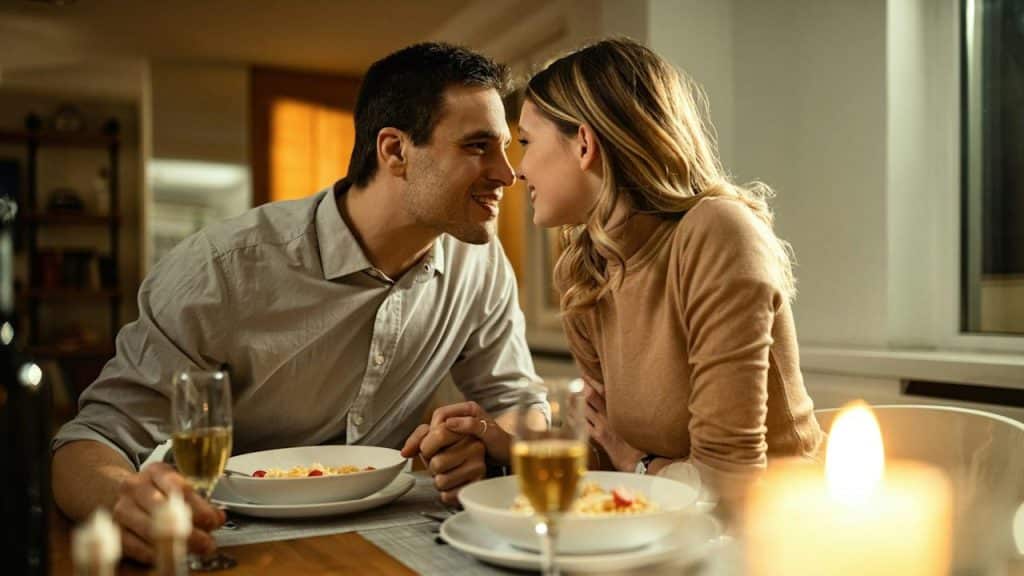 Romantic couple about to kiss while holding hands during dinner at the dining table.