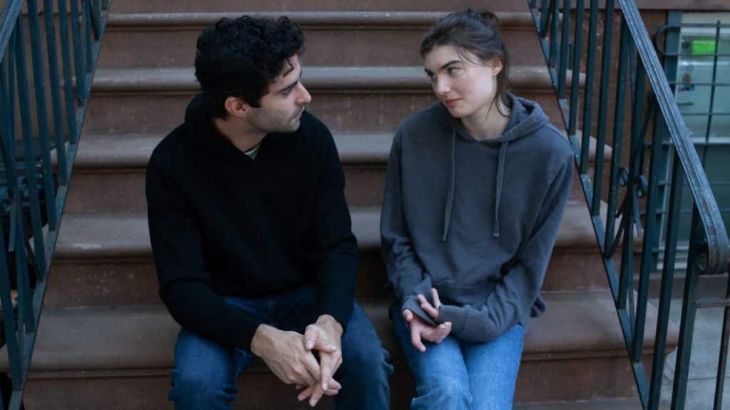 A man in a black hoodie and a woman in a grey hoodie sit on stairs.