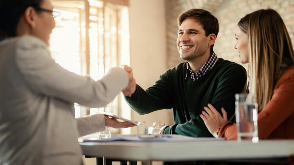 A man smiles while shaking hands with someone across a table.