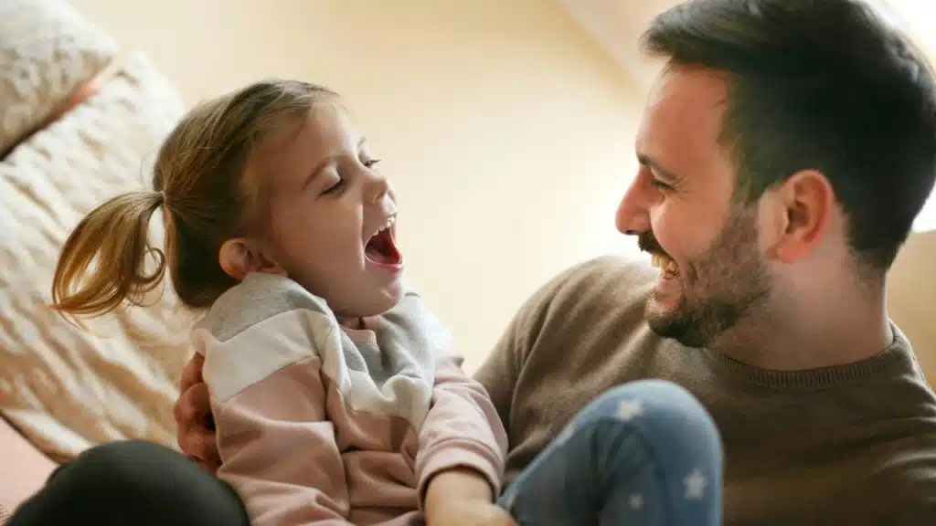A laughing man holds a young girl who is also laughing and looking up at him.