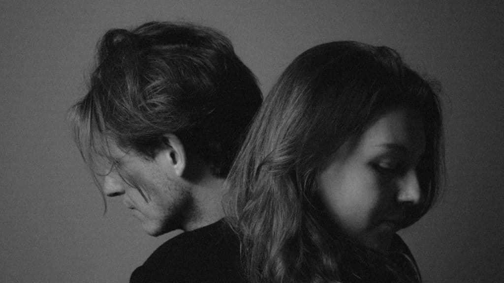 A couple standing with their backs to each other and looking downwards.
