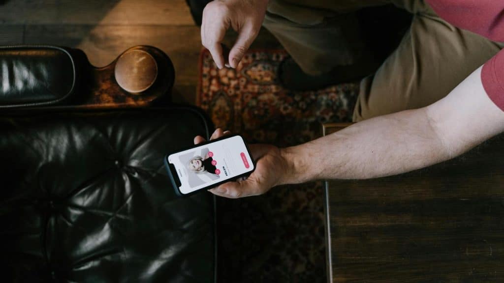 A man holding a phone showing a dating app profile.