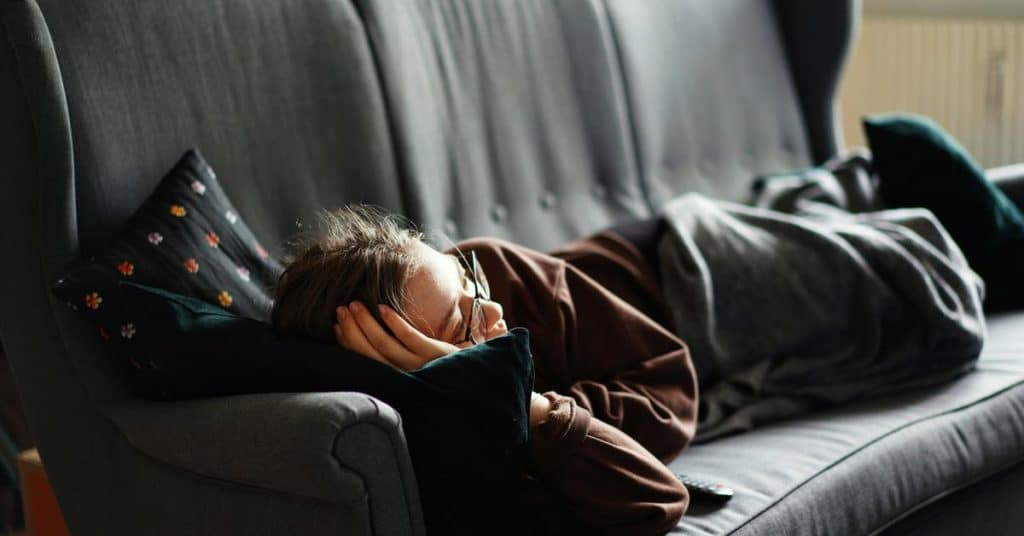 A person lies curled up on a couch resting their head on a pillow.