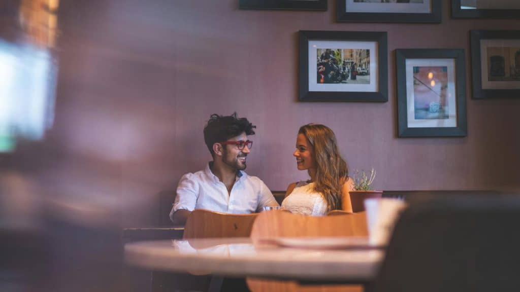 A couple smiling at each other while sitting together in a cozy café.