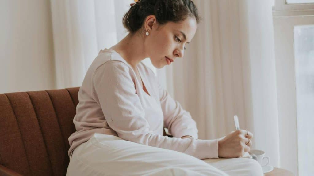 A woman sitting on a couch writing in a notebook.