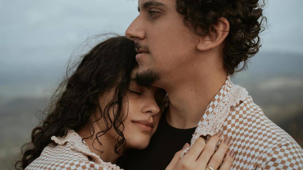 A couple embracing outdoors, wrapped together in a checkered blanket.