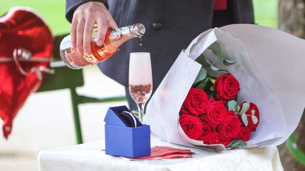 A person pours sparkling wine into a glass next to a bouquet of red roses.