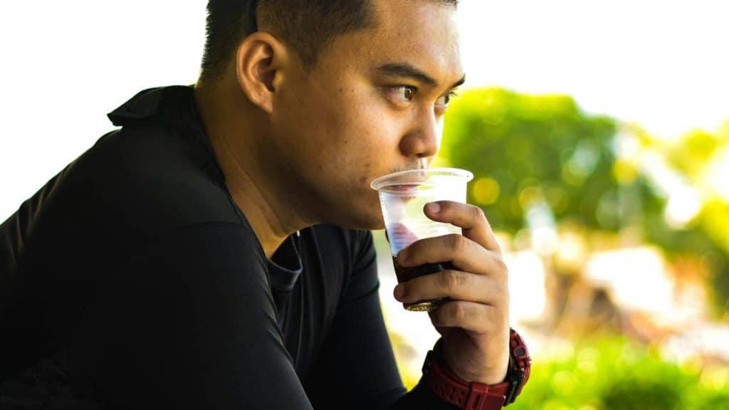A man drinking from a plastic cup while looking into the distance.