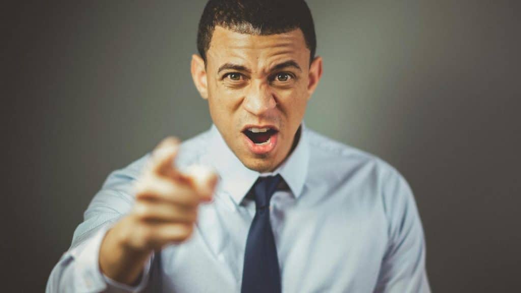 An angry man in a dress shirt pointing and shouting.