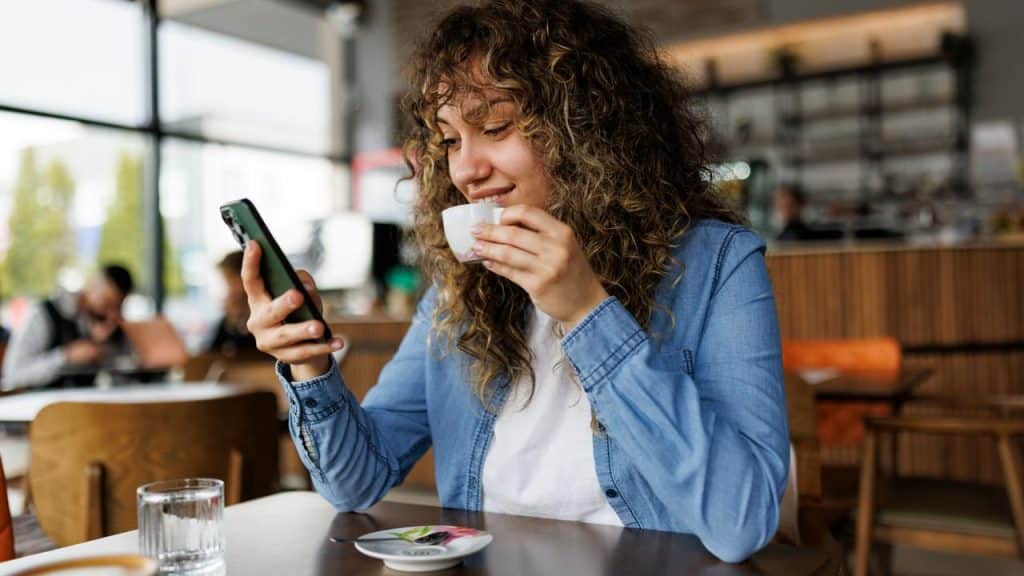 A woman checking her phone while sipping coffee at a café table.