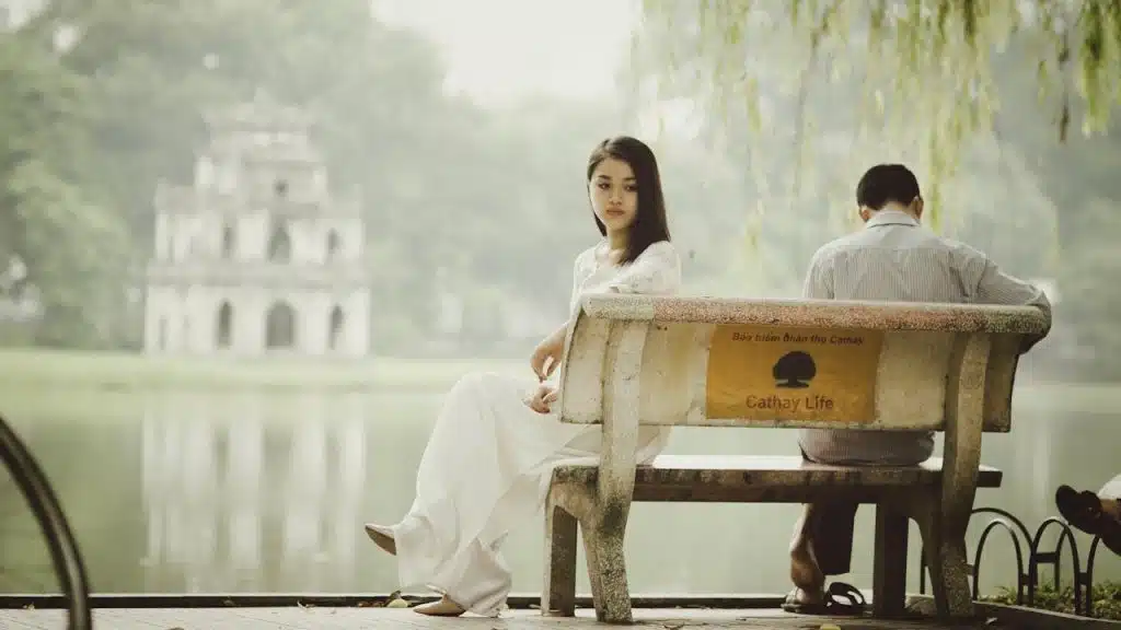 Man and woman sitting on a bench by a body of water.