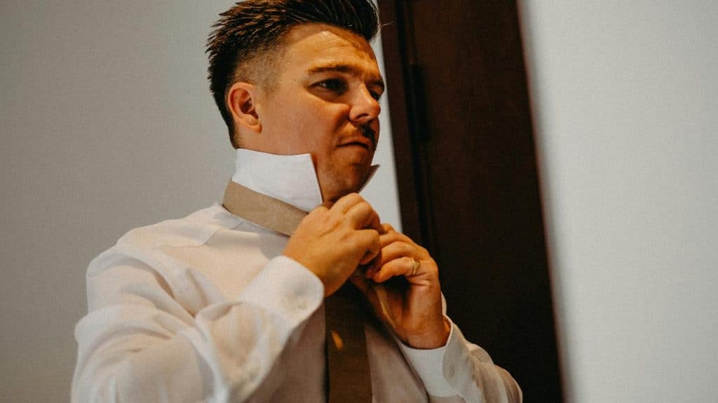 A man adjusting his tie while getting dressed indoors.