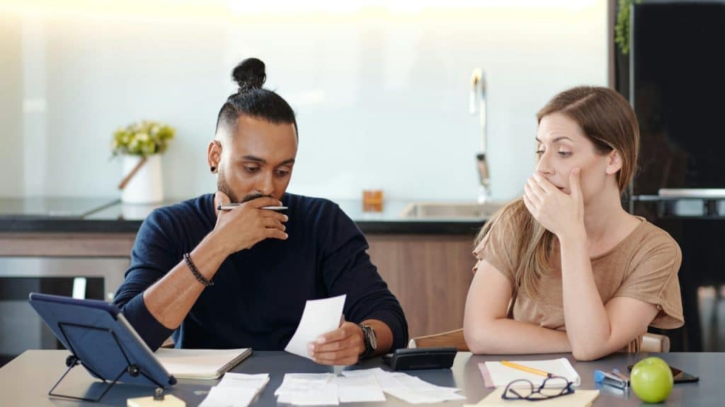 A man and woman sit at a table looking at papers, a tablet, and calculator.