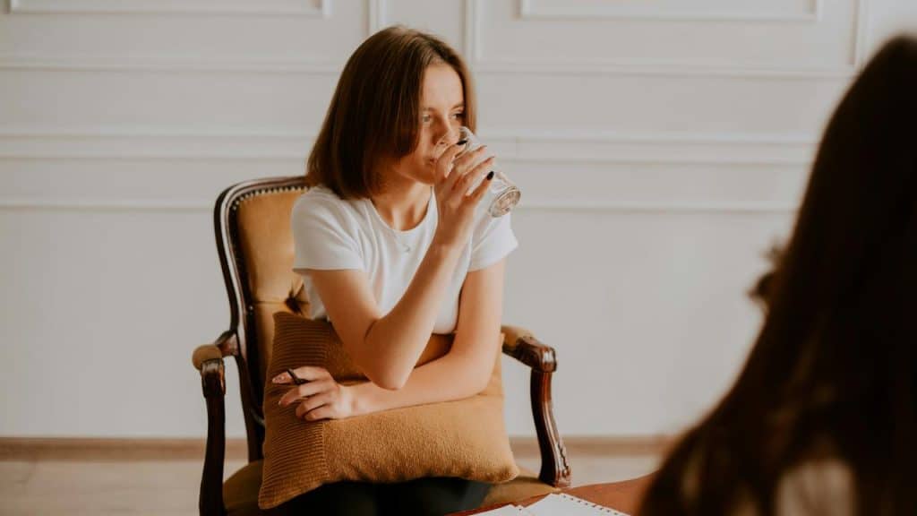 A woman sitting in a chair, sipping water from a glass.