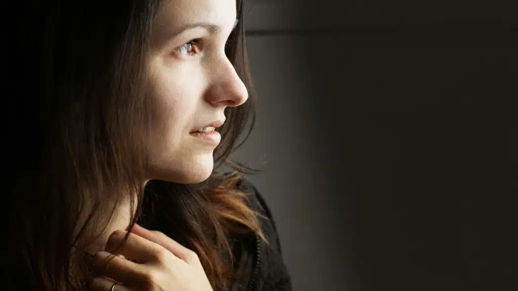 A side-profile portrait of a woman with dark hair gazing thoughtfully toward soft light.