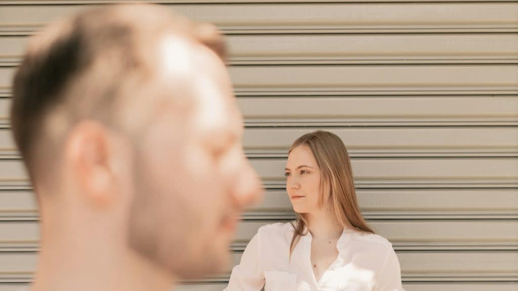 A couple standing outdoors are looking away from each other.