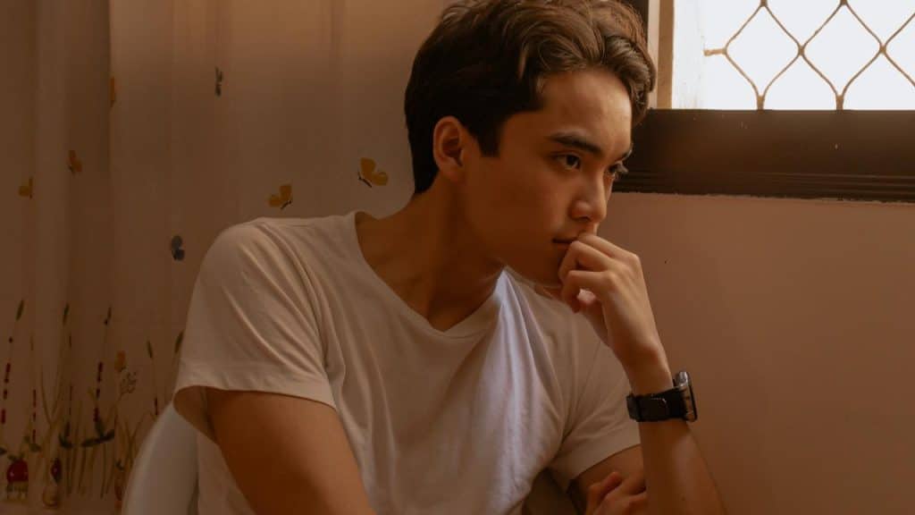 A young person sitting by a window, resting their chin on their hand in thought.