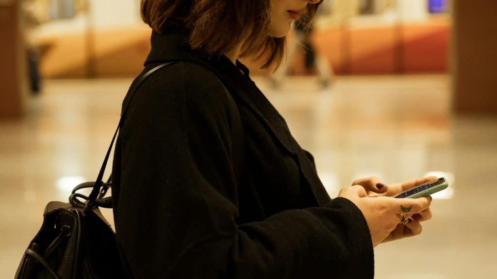 A woman in a black coat using her smartphone indoors.