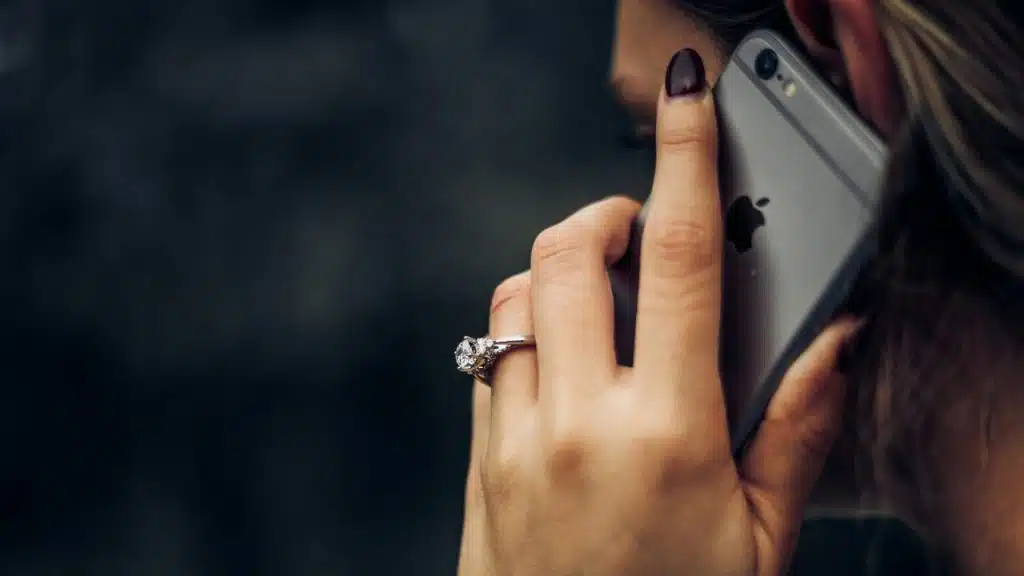 A close-up shows a hand with a ring holding a smartphone to a person's ear.