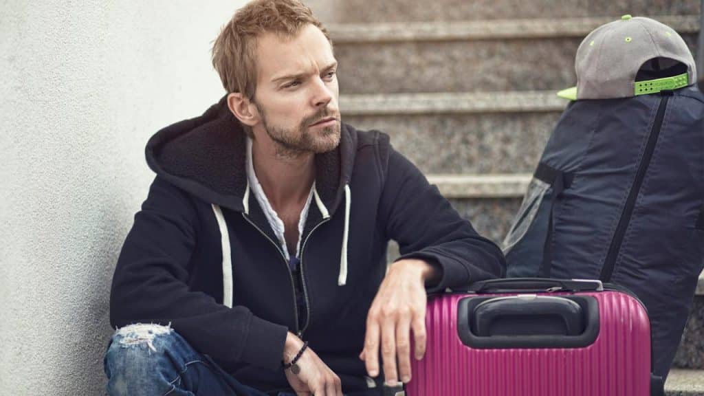 A sad man sitting on stairs with a purple suitcase.