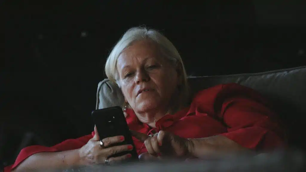 A woman in a red long-sleeve shirt holding a black smartphone.