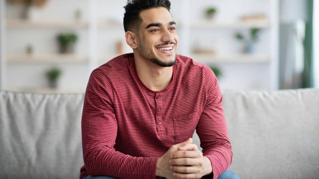 A smiling man sitting on a couch in a bright living room.