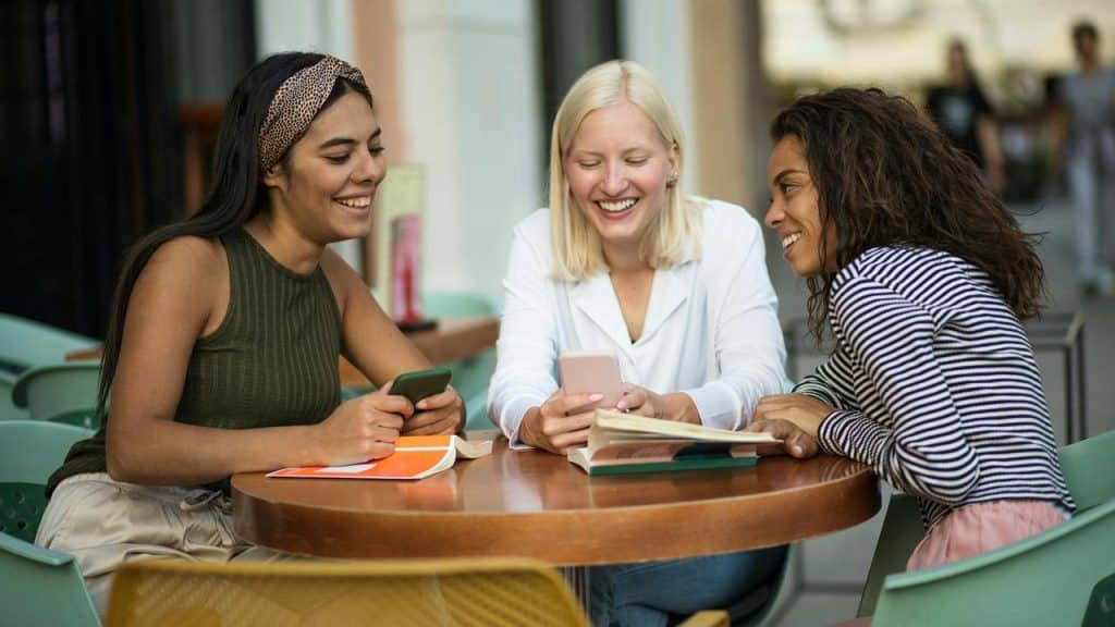 A group of friends laughing together while looking at a phone at an outdoor café.