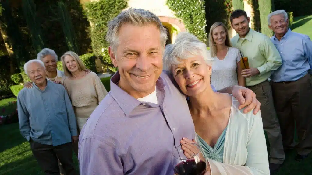 A group of smiling people of various ages pose together outdoors on a green lawn.