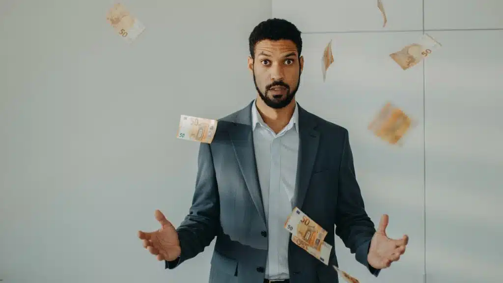 A serious young businessman standing in office throwing money away.