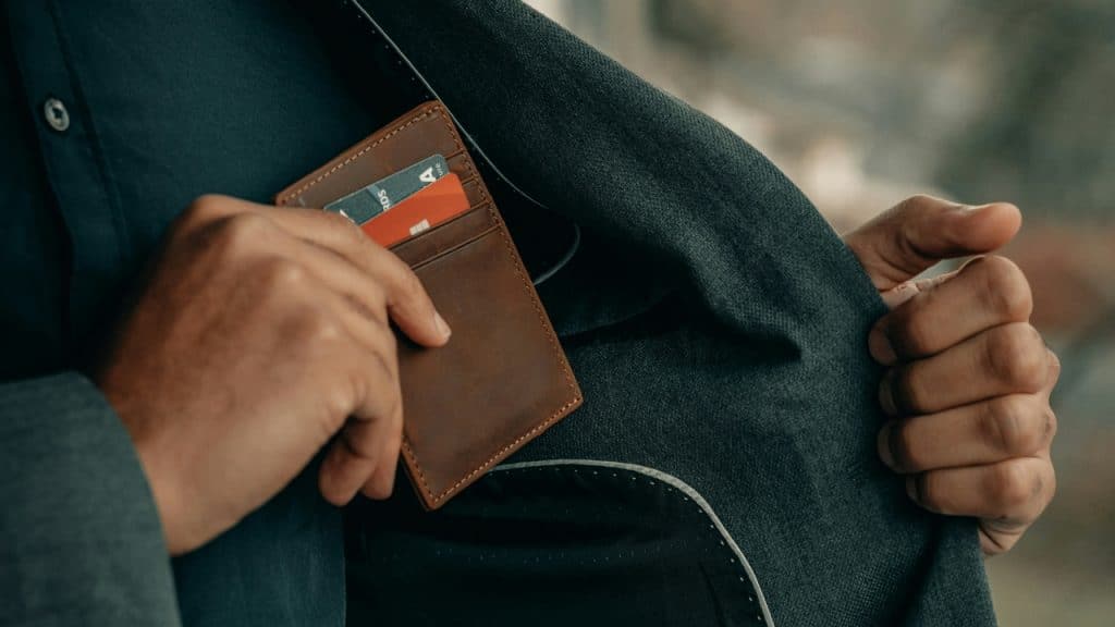 A person wearing a dark blazer reaches into an inside pocket for a leather wallet.