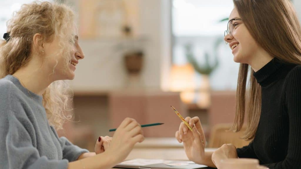 A pair of women smiling and talking while working together at a table.