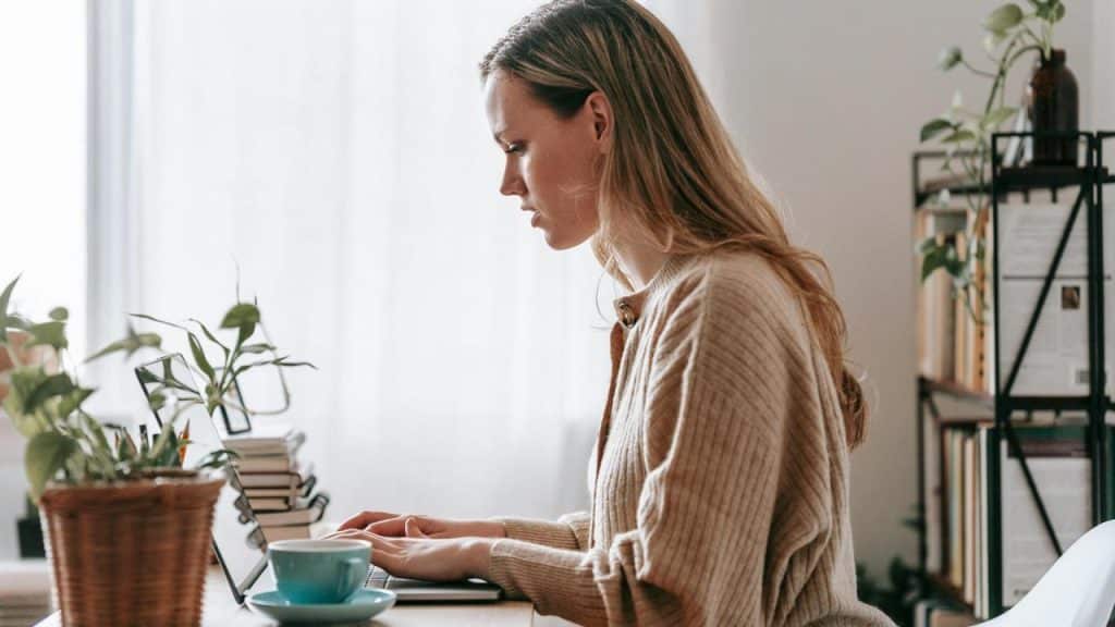 A woman working on a laptop at a desk with plants.