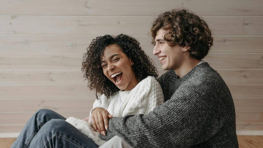 A couple laughing together while sitting closely indoors.