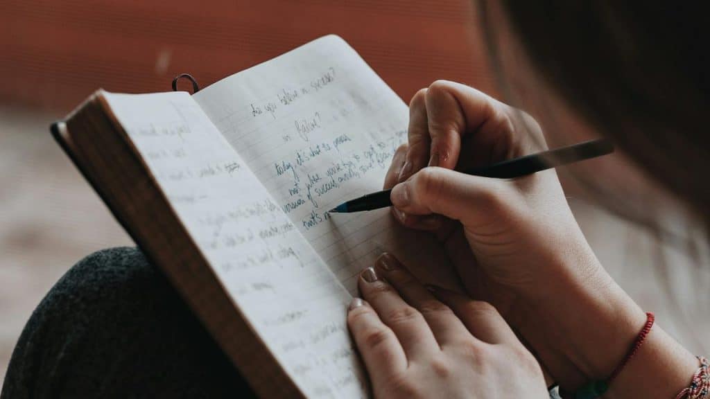 A person writing in a notebook with a pen.