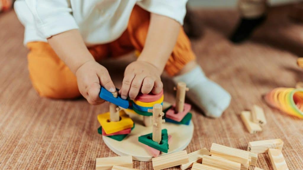 A child playing with colorful wooden stacking toys on the floor.