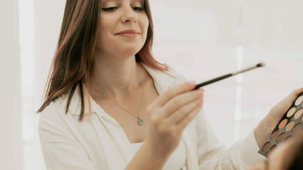 A woman applying makeup with a brush and palette.