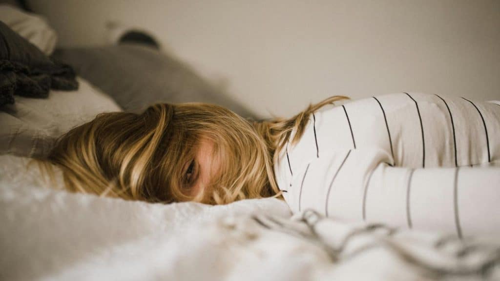 A woman lying on a bed with her face partially hidden by her hair.