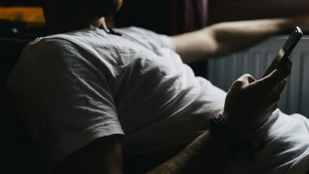 A person in a white t-shirt reclines while holding a smartphone.