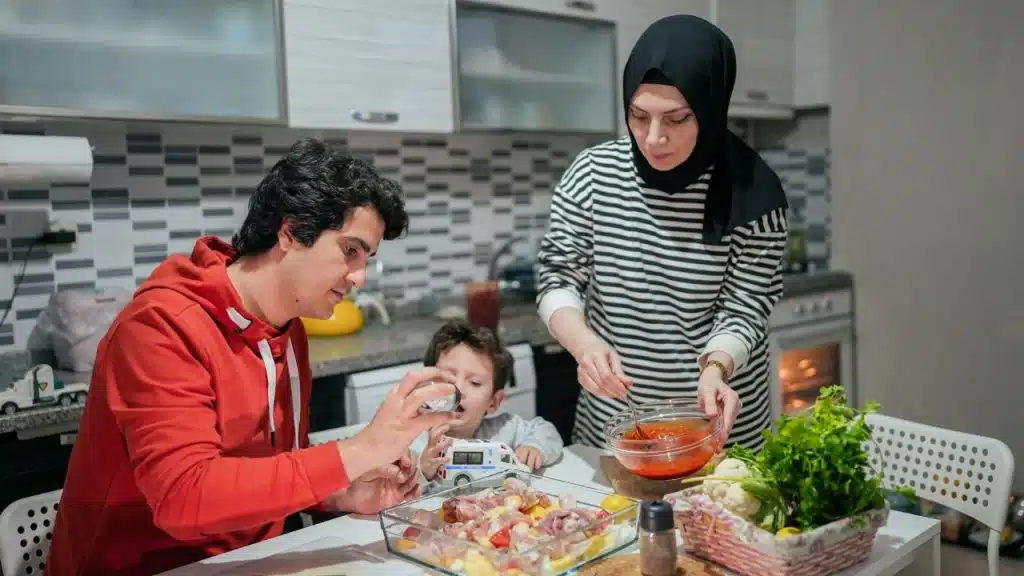 A man, woman, and child prepare a meal with chicken and vegetables in a kitchen.