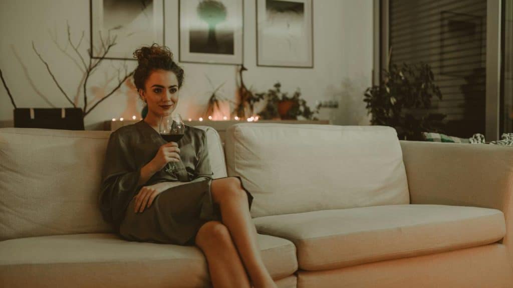 A woman sitting on a couch holding a glass of wine in a cozy living room.