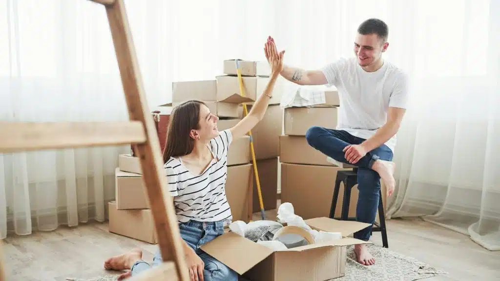 A couple high-fiving while unpacking boxes in a bright room.