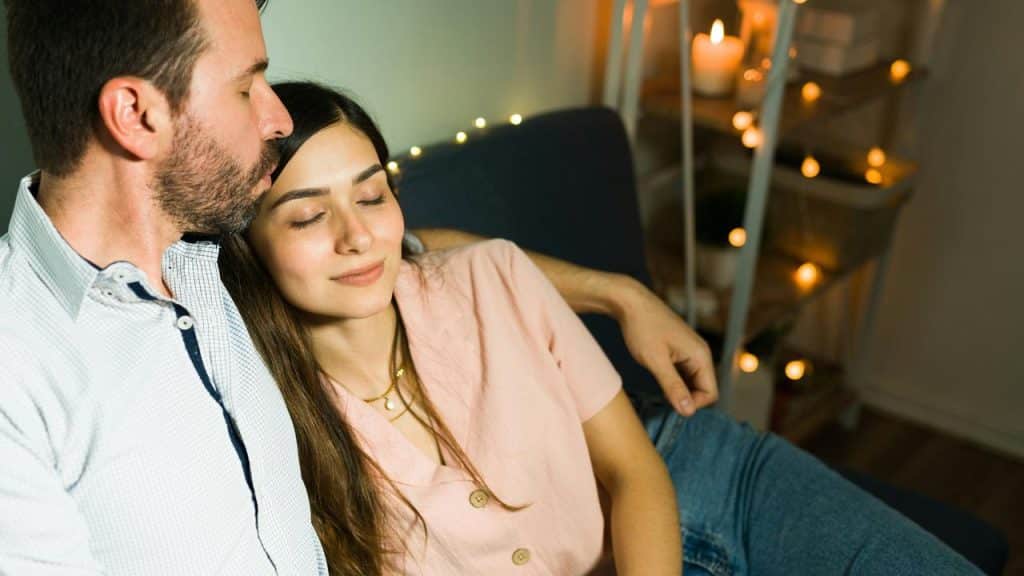 A couple cuddles on a couch with soft lights in the background.