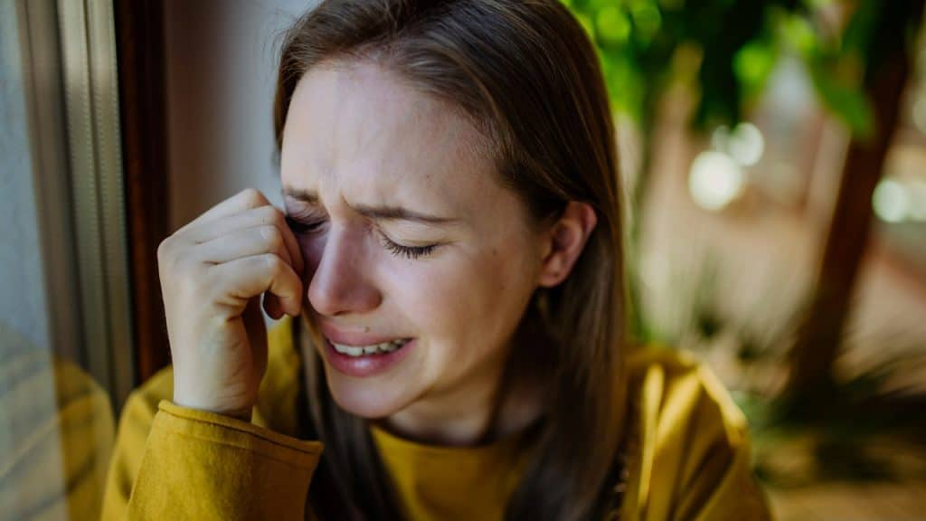 A woman is crying while sitting on a lawn.