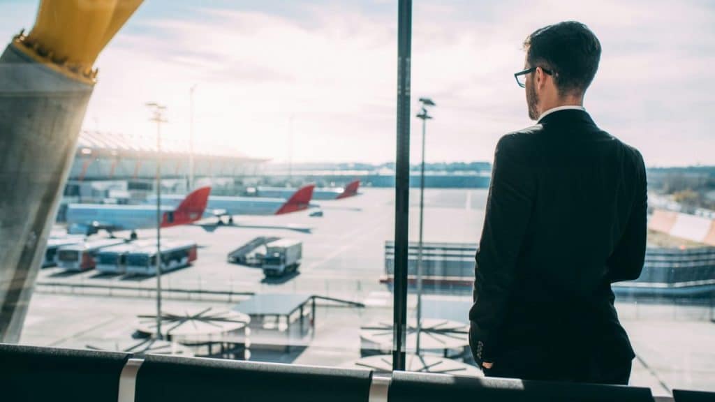 A man in a suit looking out an airport window at airplanes on the tarmac.