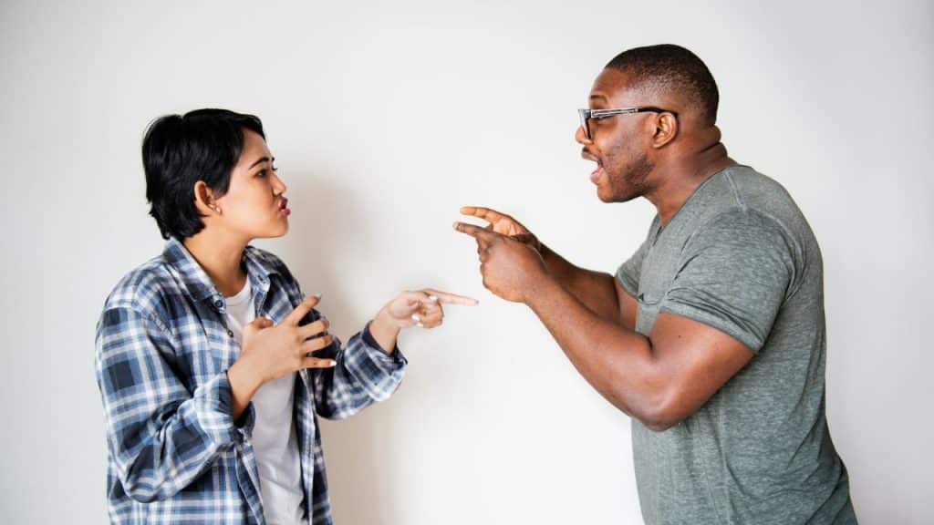 A man and woman stand facing each other, both gesturing with their hands while speaking.