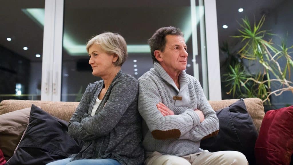 A man and woman sit back-to-back on a couch with their arms crossed.