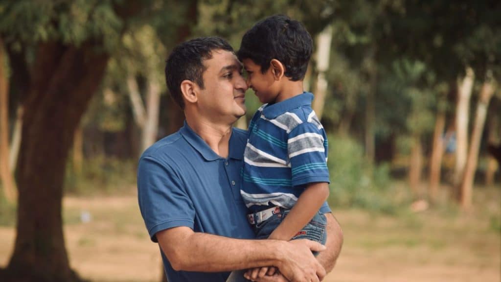 A man in a blue polo shirt holds a young boy in a striped shirt.