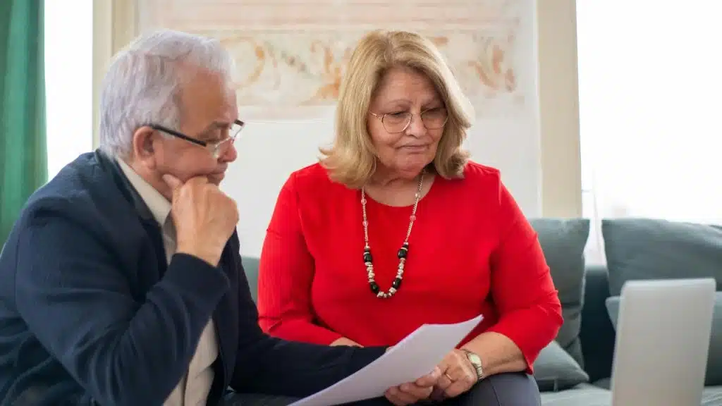 An older man and woman sit together on a sofa while reviewing a paper document.